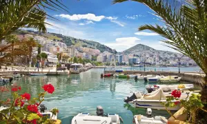 Albania - wczasy samolotem all inclusive. Widok na port z łodziami i kolorowymi budynkami na wzgórzu.