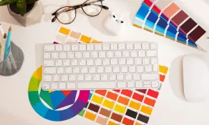 Na biurku grafika: klawiatura, myszka, okulary, słuchawki, koło barw i próbki kolorów, w tym **kolor pantone**.