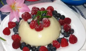 Panna cotta z malinami i borówkami, posypana cukrem pudrem. Idealny deser, który można przygotować według prostego legumina przepisu.