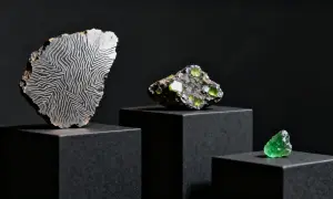 Fragmento de roca con patrón de líneas blancas sobre fondo negro, junto a cristales verdes. Explorando el cristal de roca propiedades.