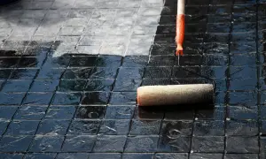 Eine Rolle versiegelt Terrassenplatten, die von dunkel glänzend zu matt wechseln.