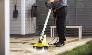 Person använder en borstmaskin för att slipa altanen. Vatten sprutar från borsten som rengör träet.