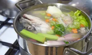 Une tête de poisson nage dans un bouillon avec des légumes, promettant un fumet de poisson savoureux.