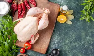 Surowy kurczak na desce z przyprawami: chili, cytryna, oliwa, pomidory, ziele angielskie, pieprz.