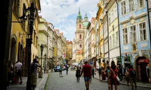 Rue pavée bordée de maisons colorées à Prague, avec une église baroque au loin. Une scène typique du top 10 des attractions de Prague.