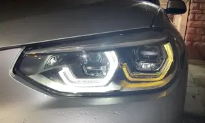 Gros plan sur un phare led qui clignote, illuminant la carrosserie mouillée d'une voiture argentée.