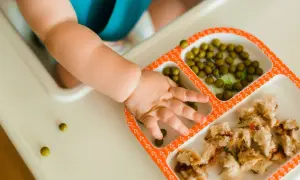 Rączka dwulatka sięga po groszek i kanapki z dżemem. Smaczna kolacja dla malucha.