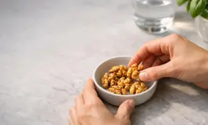 Mani prendono noci da una ciotola. Quante noci al giorno fanno bene alla salute? Un bicchiere d'acqua e basilico sullo sfondo.