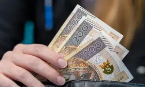 Dłoń trzyma banknoty 200 zł. Może to symbolizować wsparcie finansowe, np. stały zasiłek dla bezrobotnych po 50 roku życia.