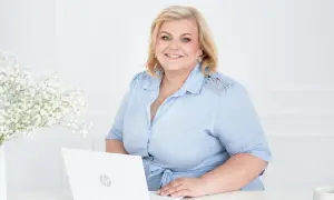 Uśmiechnięta kobieta przy laptopie, gotowa pomóc w znalezieniu pracy w Wielkiej Brytanii.