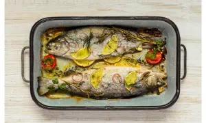 Deux truites au four, garnies de rondelles de citron, d'oignon rouge, de tomates cerises et d'herbes aromatiques, dans un plat en émail.