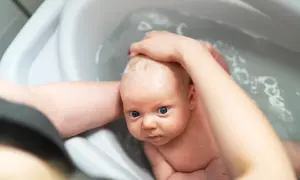 Kiedy kąpać noworodka przed czy po jedzeniu? Maluch w wanience, myty przez rodzica, z pianką na głowie.