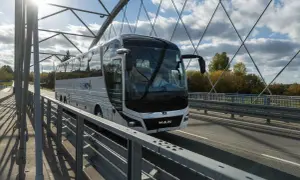 Autobus PKS NOVA na moście, podróżujący z Grajewa do Augustowa. Słoneczny dzień, chmury na niebie.