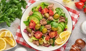 Insalata di tonno fresca e colorata con pomodori, cetrioli, olive e capperi, guarnita con limone.