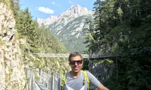 Mann auf einem Steg in der Leutascher Geisterklamm, umgeben von Felsen und Bäumen, mit majestätischen Bergen im Hintergrund.