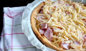 Tarta z szynką i serem, gotowa do pieczenia. Kruche ciasto, kawałki szynki i obfita warstwa startego sera.