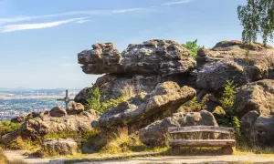 Ein Holzbank lädt zum Verweilen ein, mit Blick auf bizarre Felsen im Zittauer Gebirge und eine Stadt in der Ferne.