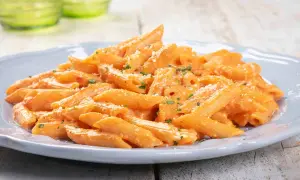 Penne cremose con salsa rosa, un classico tra le pasta ricette, guarnite con prezzemolo e parmigiano.