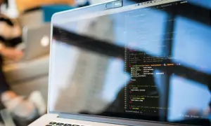 Programista kod zawodu, pisze kod na laptopie. Widać fragment ekranu z kodem w języku Ruby.