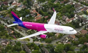 Różowy samolot Wizzair przelatuje nad osiedlem domów jednorodzinnych.