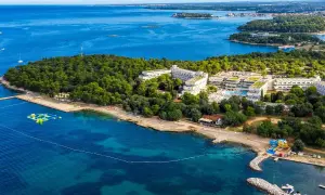 Hotel Delfin Plava Laguna, otoczony zielenią, z basenami i plażą nad turkusowym morzem.