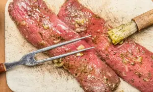 Polędwiczki wieprzowe w aromatycznej marynacie, gotowe do pieczenia. Widelec i pędzelek do sosu czekają.