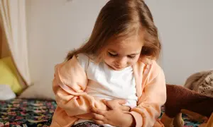 Litet barn med magsjuka och feber håller sig om magen.