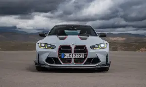 Szare BMW M4 CS z czerwonymi akcentami i agresywnym grillem, gotowe do jazdy po pustynnej drodze pod burzowym niebem.