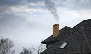 Dym wydobywa się z ceglanego komina na dachu domu.