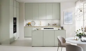 Moderna cocina verde con isla central, electrodomésticos integrados y una mesa redonda con sillas.