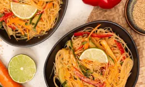 Zwei Schalen mit erfrischendem Glasnudel Salat, garniert mit Limettenspalten, Karotten- und Gurkenstreifen.