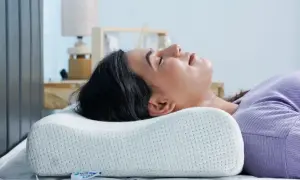 Woman sleeping on her back with head cradled by an ergonomic pillow, demonstrating the **forma correcta de dormir con almohada** for optimal neck support.