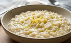 Un cremoso risotto al limone, guarnito con scorza di limone e scaglie di parmigiano, servito in una ciotola rustica.