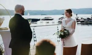 Para młoda podczas ślubu rzymskiego nad jeziorem. Panna młoda w białej sukni z bukietem, pan młody w garniturze.