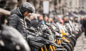 Mężczyzna w kasku ogląda lekki motocykl. W tle rząd innych motocykli i ludzi.