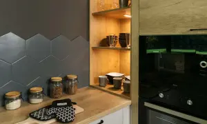 Drewniane półki do kuchni z naczyniami i słoikami z produktami. Obok piekarnik i mikrofalówka.