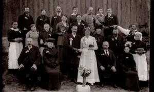 Un groupe de familles posant pour un recensement ad 88. La mariée, en blanc, tient un bouquet.