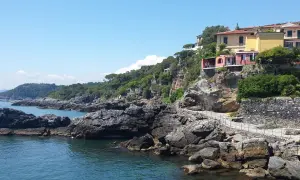 Case colorate su una scogliera rocciosa, con il mare blu e il cielo limpido. Un sentiero panoramico si snoda lungo la costa, ricordando la bellezza della riviera delle palme San Benedetto del Tronto.