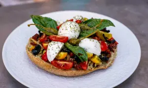 Frisches Brot belegt mit Tomaten, Kapern, Oliven und verschiedenen Mozzarella Arten, garniert mit Basilikum.