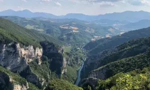 Vista mozzafiato dalla terrazza del Furlo: un fiume serpeggia tra gole rocciose e colline verdi, sotto un cielo azzurro con nuvole bianche.