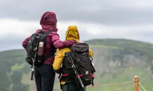 Dwie osoby w kurtkach z kapturem i plecakami patrzą na krajobraz.