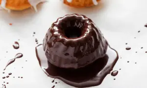 Una torta con glassa al cioccolato, lucida e invitante, con gocce di cioccolato che si spargono sul bianco.