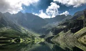 Malowniczy Czarny Staw Gąsienicowy, odbijający się w tafli wody, otoczony stromymi, skalistymi górami. Trasa widoczna na zboczu.
