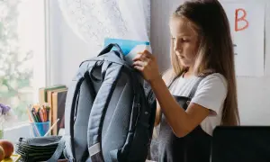 Dziewczynka wkłada książkę do plecaka. Zastanawia się, jak prać plecak w pralce, by był czysty na nowy rok szkolny.