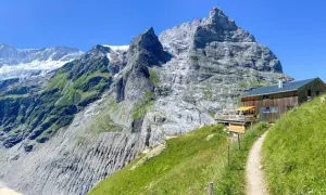 Ein Weg führt zu einer Berghütte mit Terrasse vor imposanter Schweizer Bergkulisse. Perfekt für eine Pause beim **Schweiz wandern**.