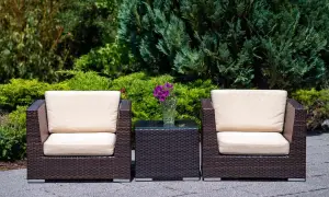 Dos sillones y una mesita de centro de ratán, perfectos para el mantenimiento de muebles de exterior. Flores moradas en un jarrón.