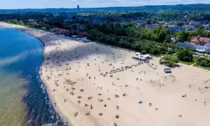 Idealny dzień, by wsiąść w pociąg i pojechać nad morze. Szeroka, piaszczysta plaża pełna ludzi, z błękitną wodą i zielonym miastem w tle.