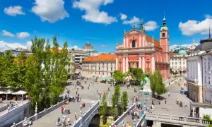 Tętniący życiem plac w Lublanie, stolicy Słowenii, z różową katedrą i mostami pełnymi ludzi.