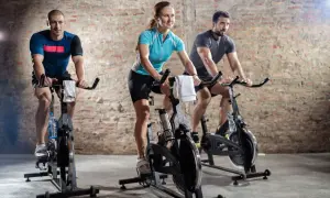 Trzy osoby ćwiczą na rowerach stacjonarnych. To jest właśnie spinning – intensywny trening kolarski w grupie.