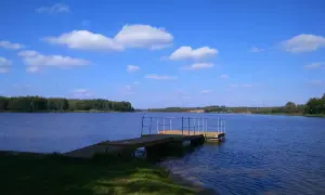 Drewniana przystań na spokojnym zalewie Drzewica. Błękitne niebo z białymi chmurami nad taflą wody i zielonymi lasami w tle.